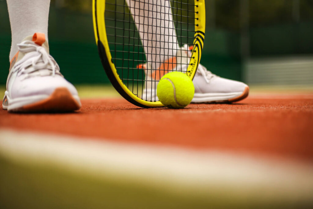 Detailaufnahme: Tennisball neben Tennisschläger und Turnschuhen