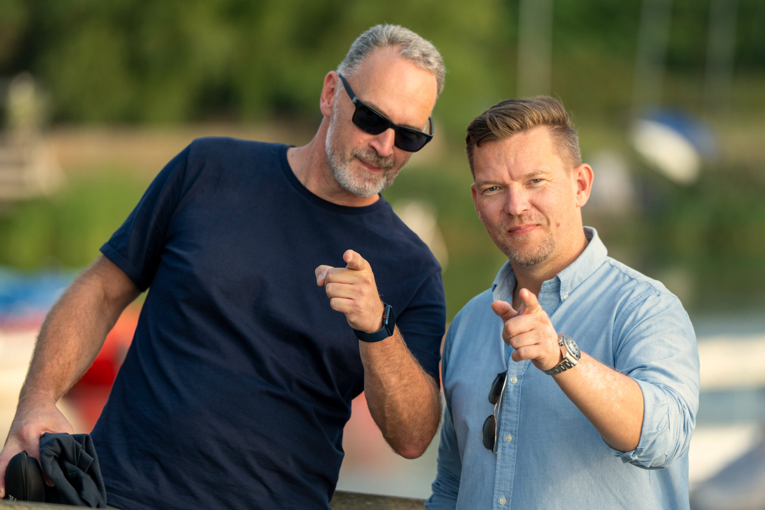 4M-Kollegen schauen in die Kamera und zeigen direkt auf Betrachter des Bildes